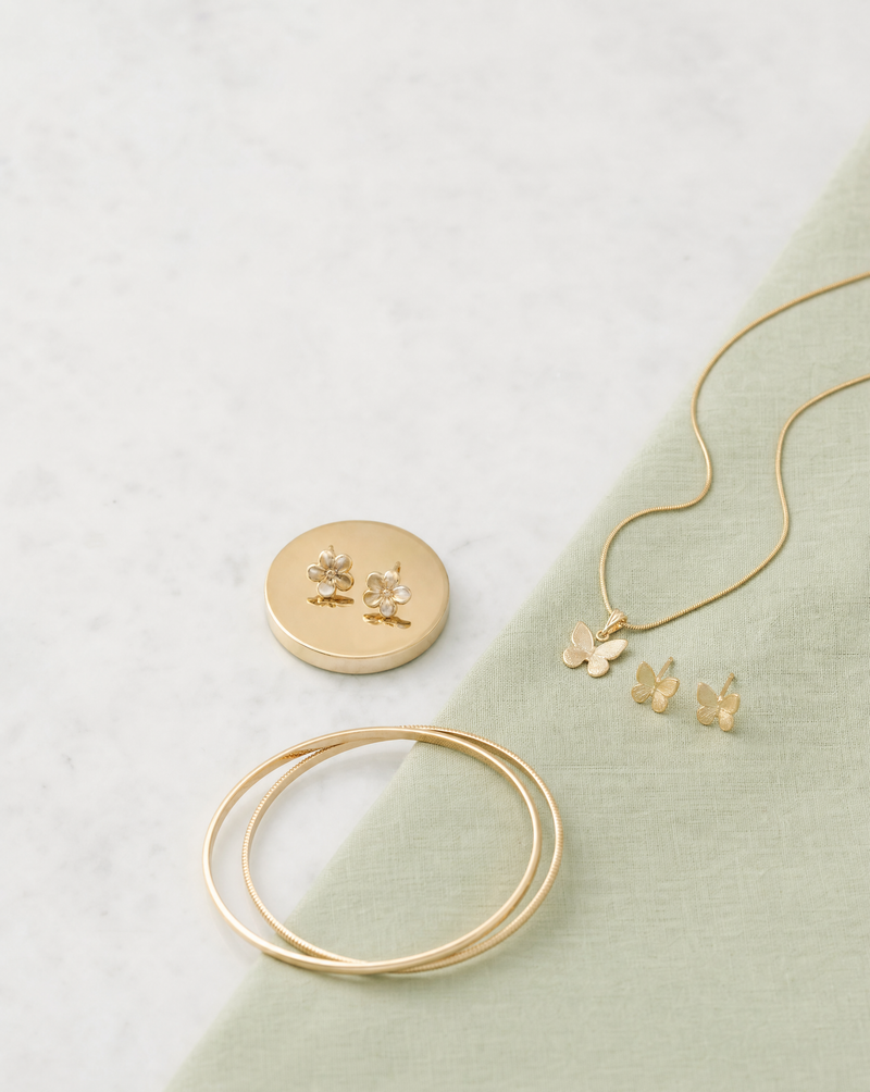 Koncept99 - gold-tone earrings on a coin, butterfly pendant set and bangles on sage linen